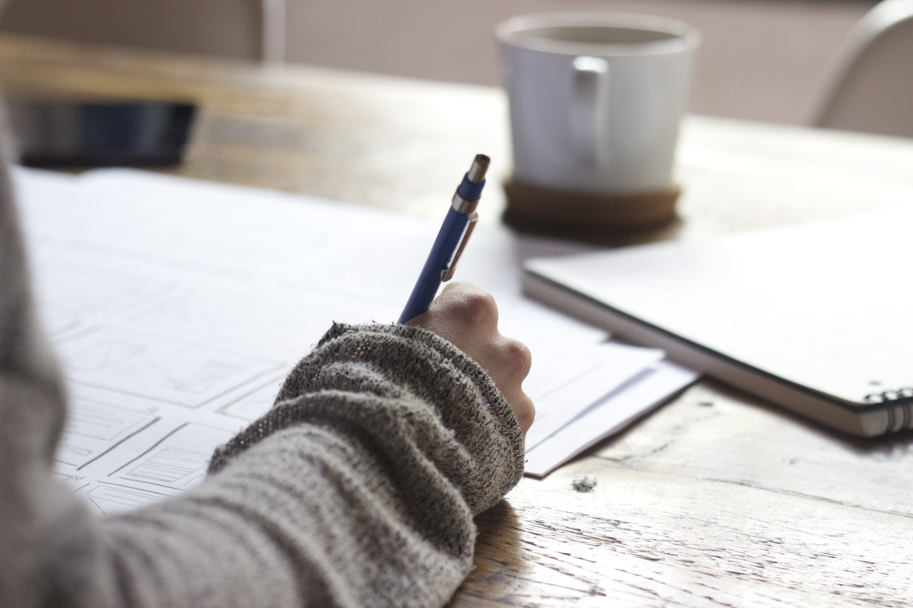 rechterhand en onderam met pen en papier op houten tafel met kopje koffie